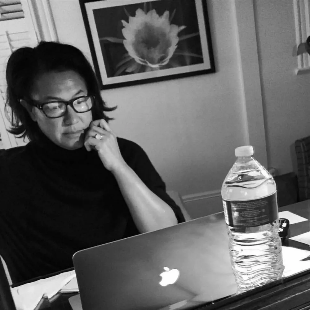 Black-and-white photo of Scilla at her laptop, in glasses, chin resting on her hand, deep in thought.